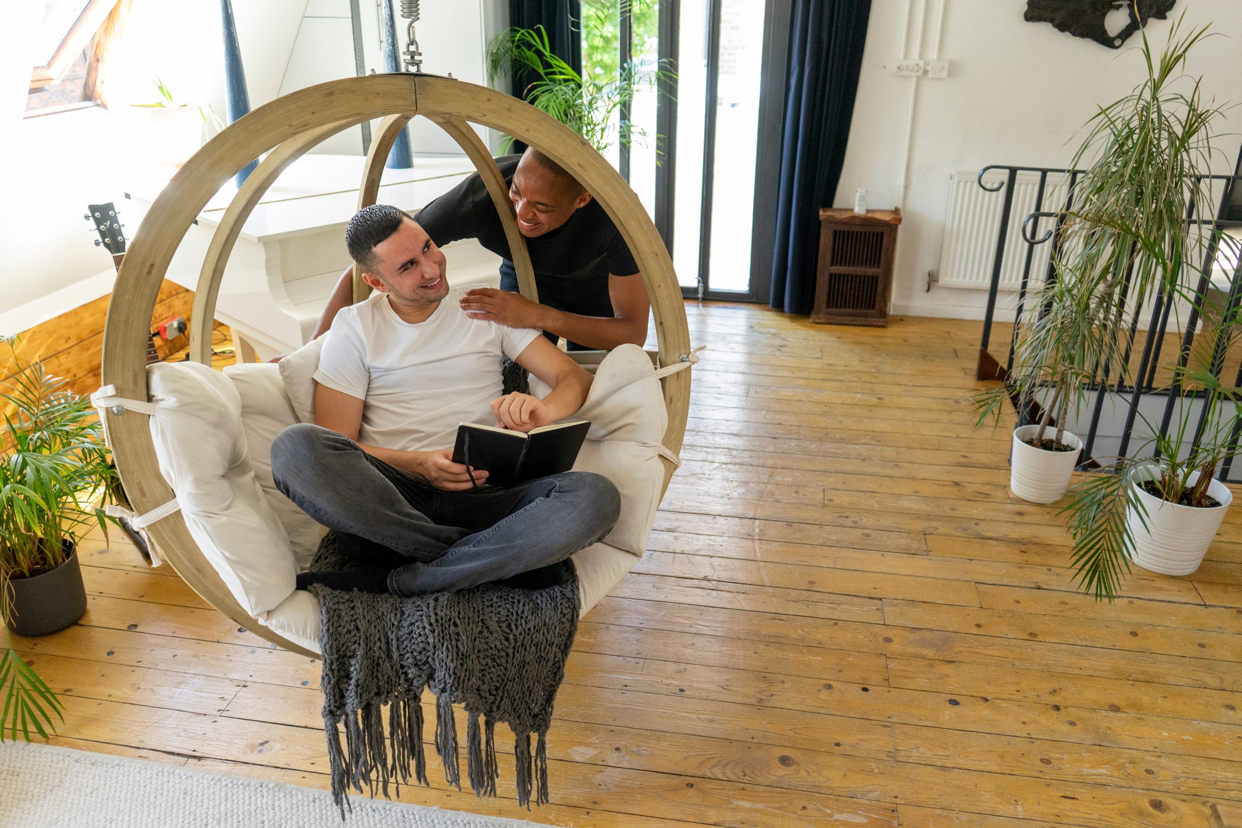 Eco-Friendly Wood Floor Sanding in London – Isleworth loft with reclaimed pine floorboards restored to a warm finish as a couple relaxes on a hanging chair.