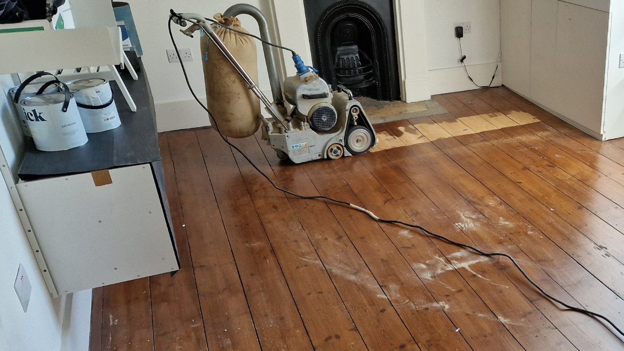 Floor sanding machine in action on Victorian pine floorboards during Transforming Victorian Boards, showing mid-restoration progress in a period living room.