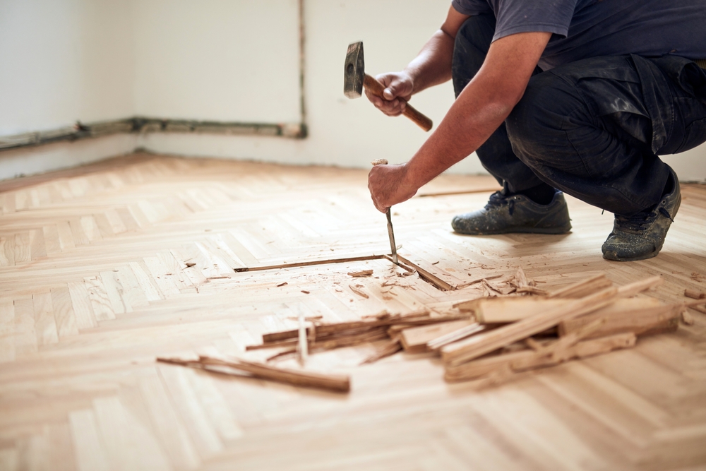 Heritage Parquet repair in Isleworth — technician removing damaged oak herringbone parquet solid-wood blocks with chisel and hammer before relay.