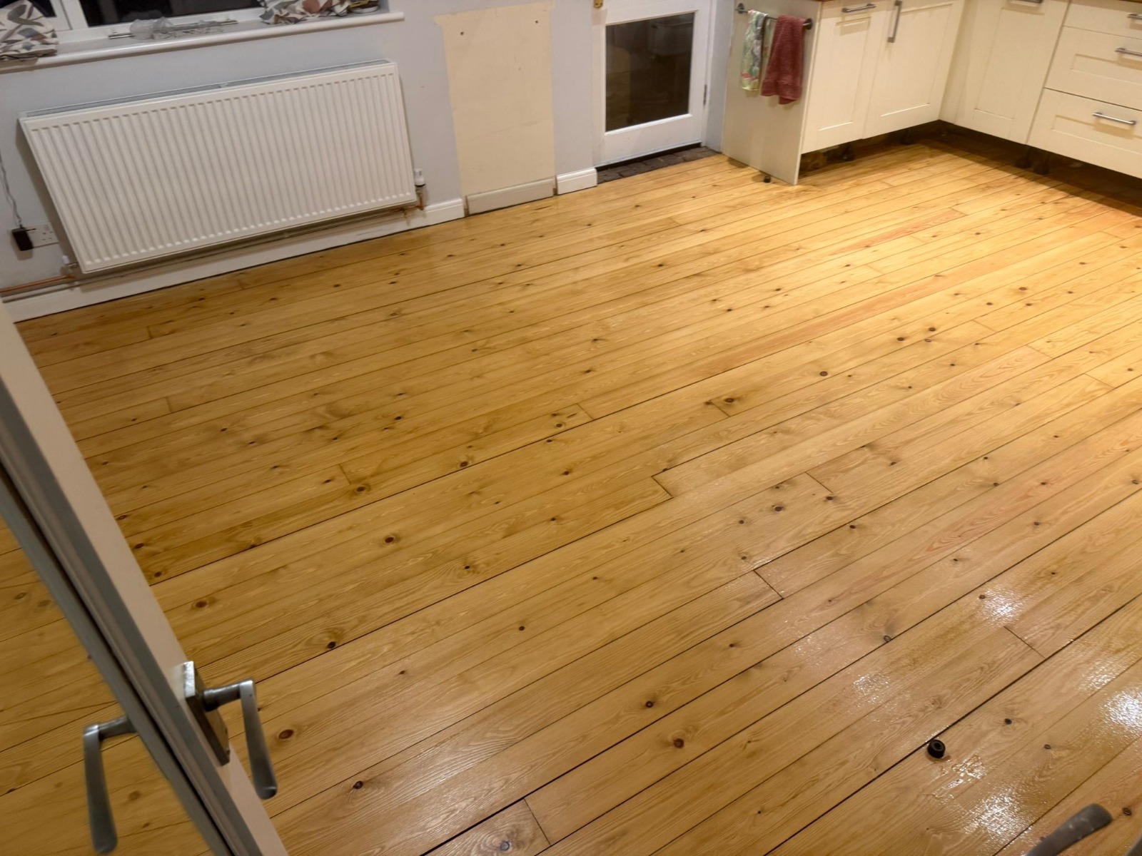 Completed Wood Floor Sanding in an Isleworth kitchen, showing smooth, sealed softwood pine floorboards with a warm, glossy finish.