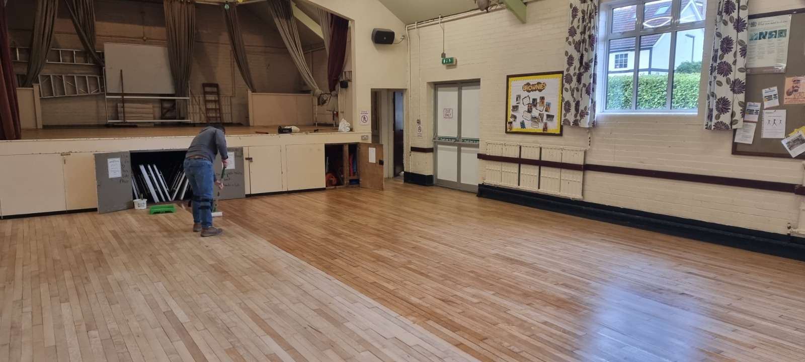Commercial Wood Floor Sanding in an Isleworth community hall, with a technician sealing freshly sanded maple strip hardwood flooring to a warm, even finish.
