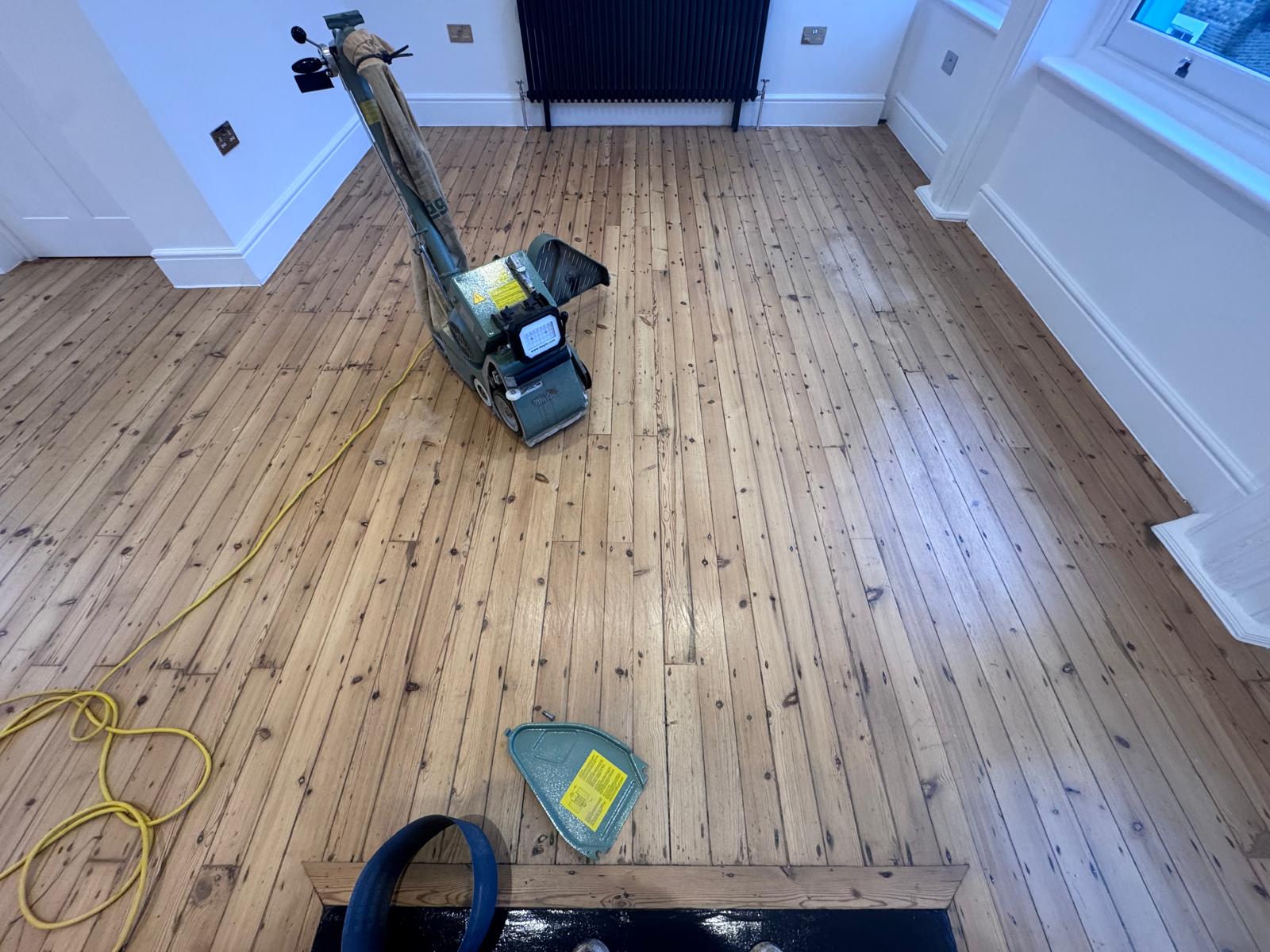 Wood Floor Sanding in Isleworth living room with professional belt sander working on original pine floorboards, leaving a smooth, freshly sanded softwood surface.